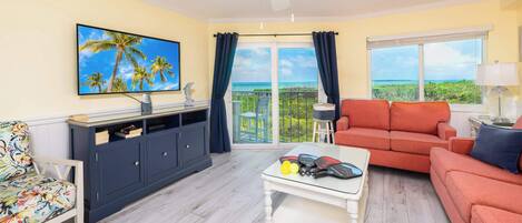 A living room with a TV, sofa, coffee table, and a balcony with a view.