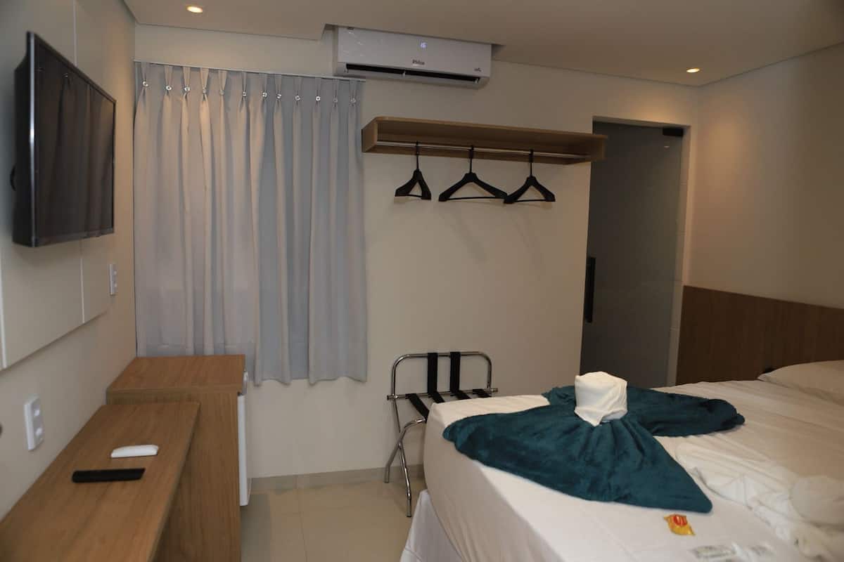 Habitación de hotel con cama, escritorio, televisor, armario y zona de ducha.