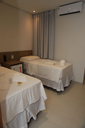 A hotel room with two beds, a nightstand, a small table, and an air conditioning unit.