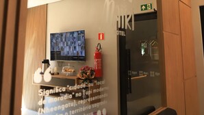 Ein Hotel-Empfangsbereich mit modernem Design, einem Fernsehbildschirm, einem Feuerlöscher und einer Wand mit einem Zitat.