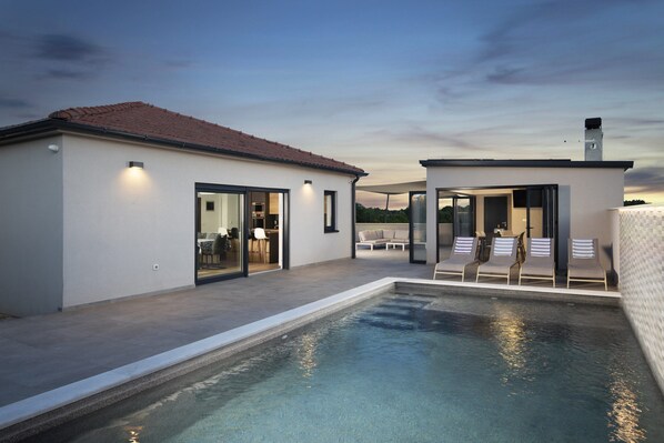 Ein modernes Haus mit Swimmingpool, einer Terrasse mit Liegestühlen und einem überdachten Sitzbereich im Freien.