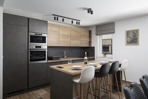 Eine moderne Küche mit eingebauten Geräten, eine Holz-Kücheninsel mit Barhocker und ein Essbereich mit Fenster.