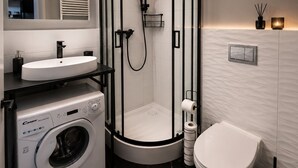 Une salle de bain moderne avec une douche à parois de verre, un lave-linge encastré, un lavabo et des toilettes.