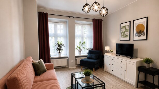 Un salon comprenant un canapé, un fauteuil, un téléviseur, un meuble et deux fenêtres avec des rideaux.