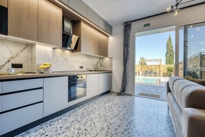 A modern kitchen with a marble countertop, wooden cabinets, and a view of a pool and outdoor seating. - Nightingale Alexander Villa - private pool (Paleokastritsa)
