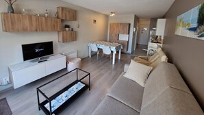 Een moderne woonkamer met een flatscreen televisie, een bank, een salontafel en een eethoek met een tafel en stoelen.