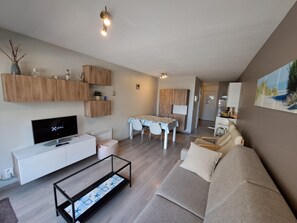 Ein modernes Wohnzimmer mit Flachbildfernseher, einer Couch, einem Couchtisch und einem Essbereich mit Tisch und Stühlen.