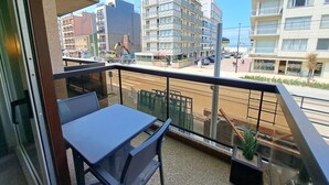 Een balkon met een tafel en stoelen, uitkijkend op een straat met gebouwen en geparkeerde auto's.