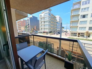 Ein Balkon mit Tisch und Stühlen mit Blick auf eine Straße mit Gebäuden und parkenden Autos.
