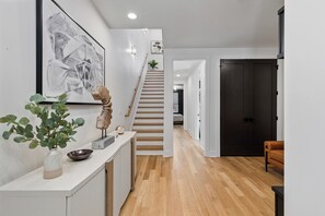 Ein modernes Interieur mit Treppe, einem weißen Konsolentisch, einer Pflanze und einer dunklen Tür.