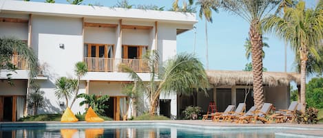 A modern hotel with a pool, lounge chairs, and palm trees.