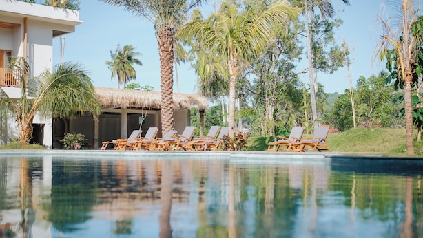 A pool area with lounge chairs, a thatched-roof structure, and palm trees. - Giri Rose Boutique Hotel (Kuta)