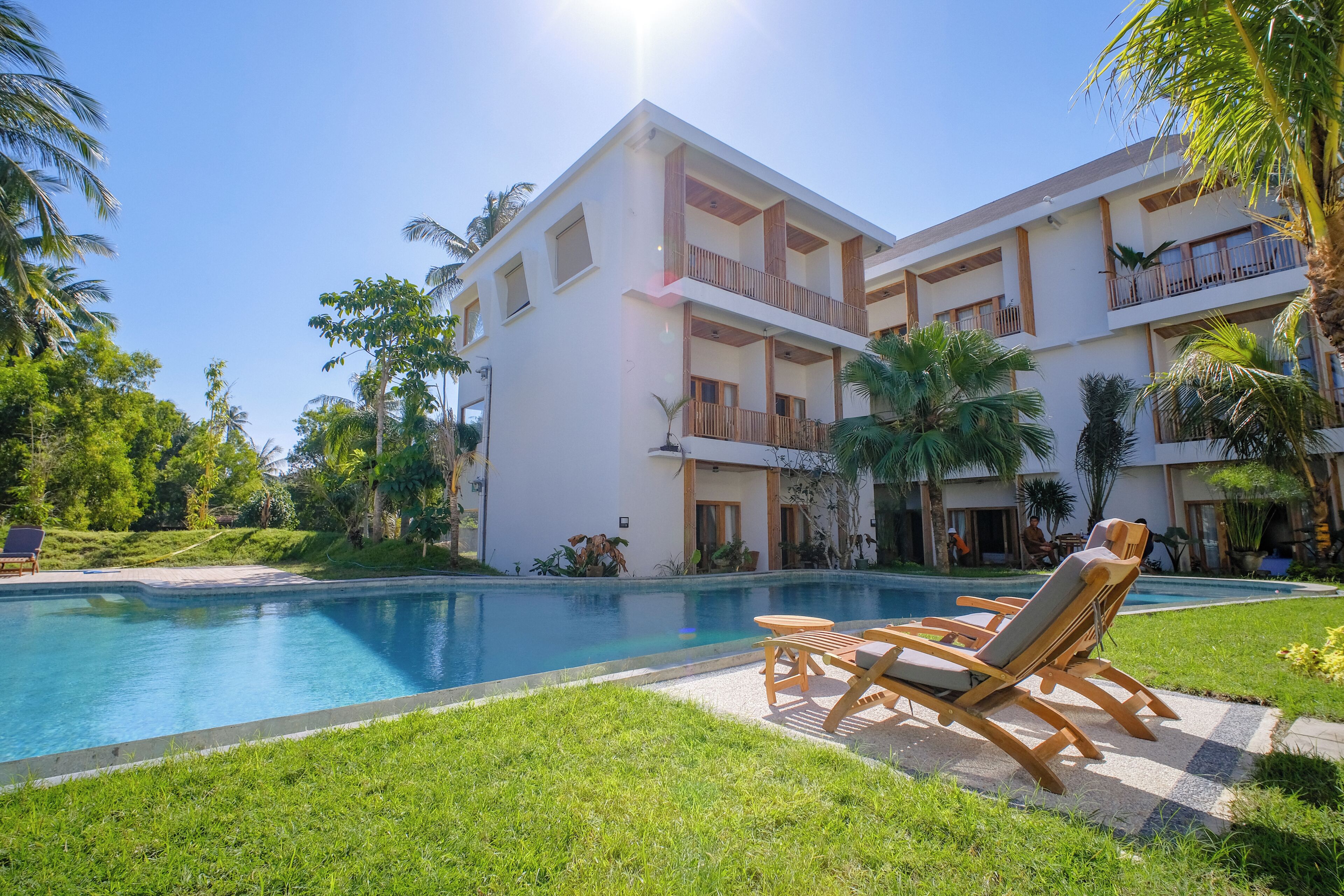A modern hotel with a swimming pool, outdoor seating, and lush greenery.