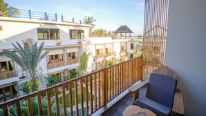 A balcony with wooden railings, a cushioned seating area, and a view of a multi-story building with balconies and potted plants. - Giri Rose Boutique Hotel (Kuta)