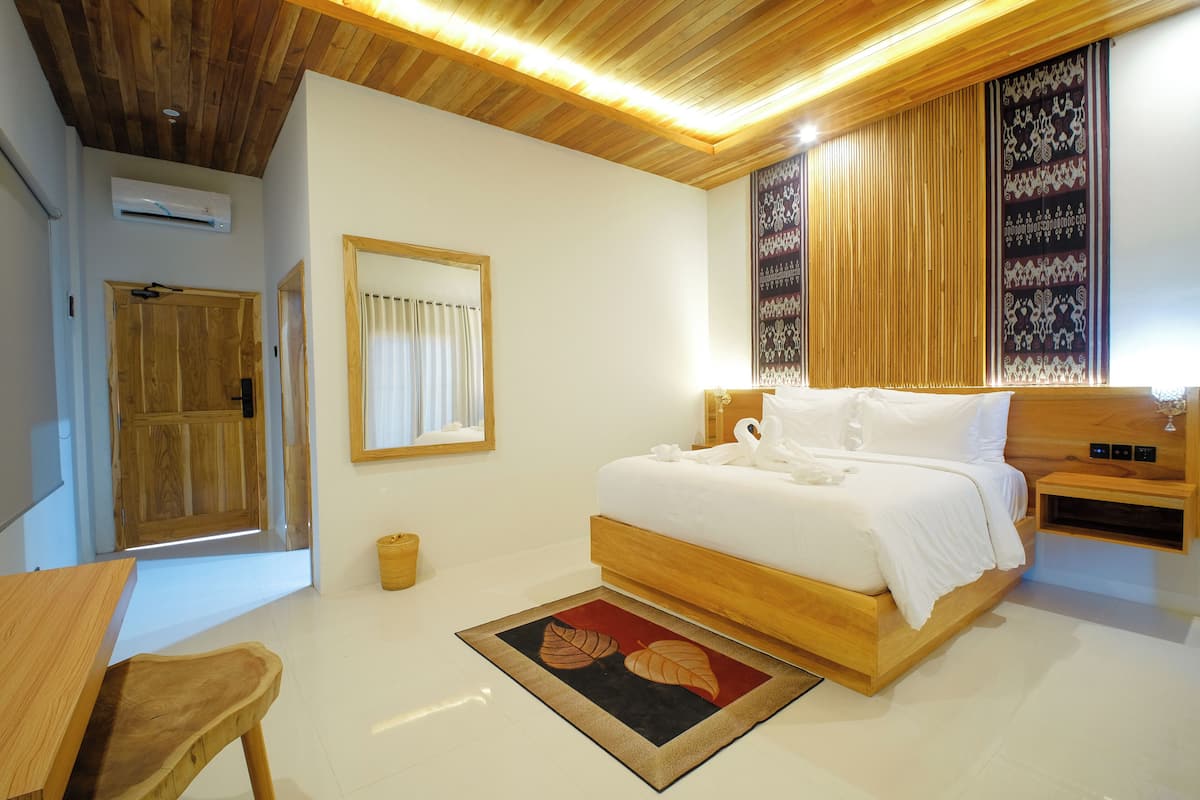 Une chambre avec un plafond en bois, un lit avec une literie blanche, une table de chevet en bois, une porte en bois et un tableau encadré accroché au mur.