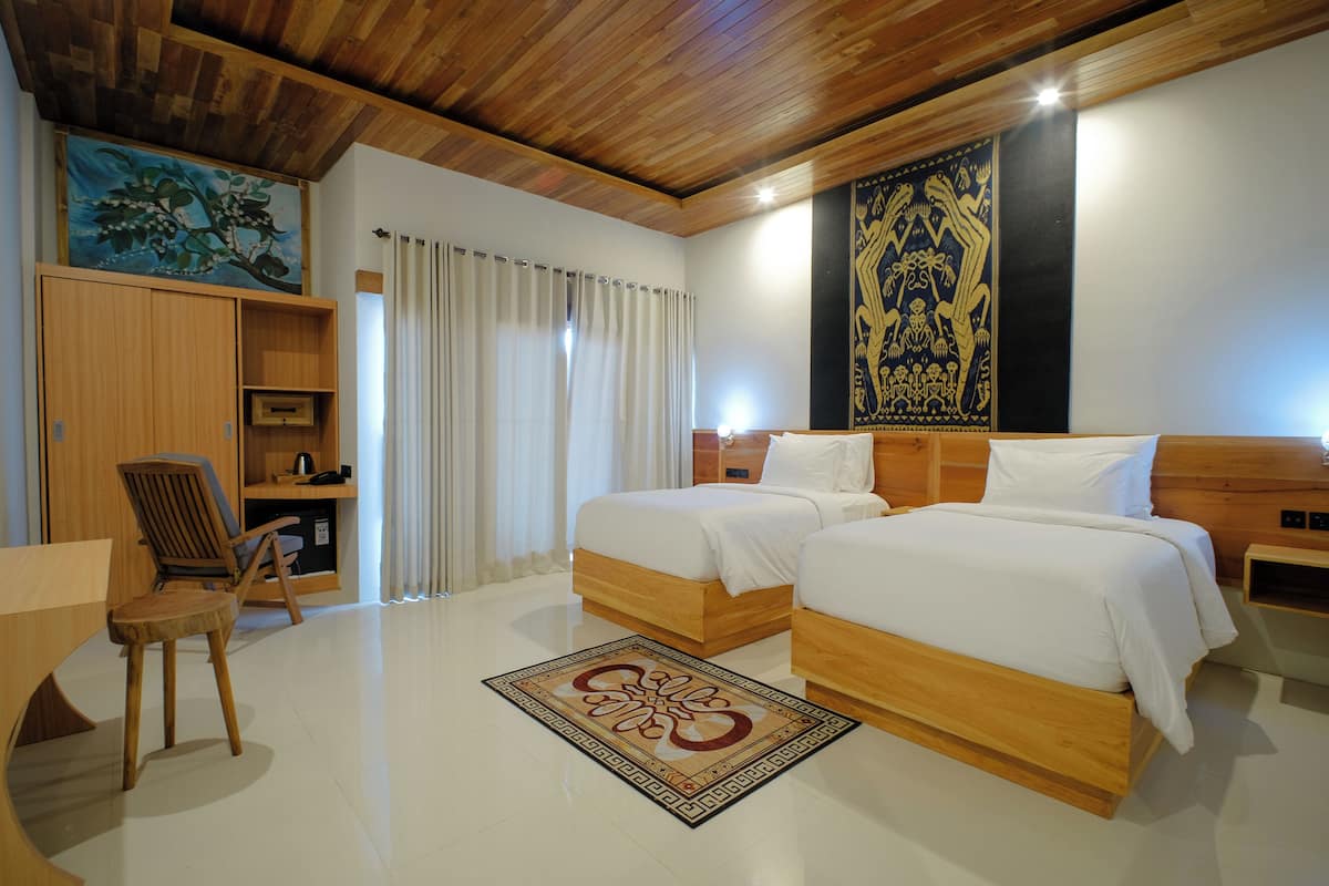 Une chambre d’hôtel avec deux lits en bois, un bureau avec une chaise, une grande fenêtre avec des rideaux et un plafond en bois.