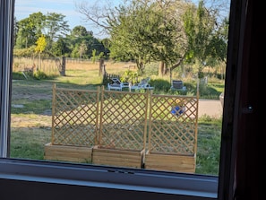 Blick durch ein Fenster auf einen Raum mit einer Holztrennwand, eine kleine Holzbank und einen Einblick in eine Außenbestuhlung.