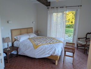 A bedroom with a bed, bedside tables, a chair, and a view of greenery through a window. - Maison Millefeuille Bed and Breakfast: Between the Forest and the Marshes, Just 10 Minutes from the Beaches! (Saint-Hilaire-de-Riez)