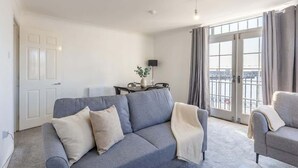 A modern living room with a grey sofa, a smaller grey armchair, and a dining table with chairs. - Modern 2BR Sea View Flat on the Harbour (Whitehaven)