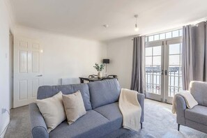 Una sala moderna con un sofá gris, un sillón gris más pequeño y una mesa de comedor con sillas.