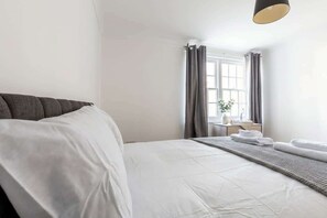 Una habitación de hotel con cama, una mesita de noche con lámpara y una ventana con cortinas.
