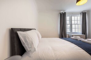 Une chambre d’hôtel avec un lit, une table de chevet, une fenêtre avec des rideaux et une lampe.