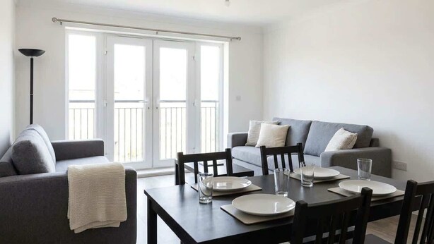 A dining area with a table set for four, a sofa, and a window with a view. - Modern 2BR Sea View Flat on the Harbour (Whitehaven)