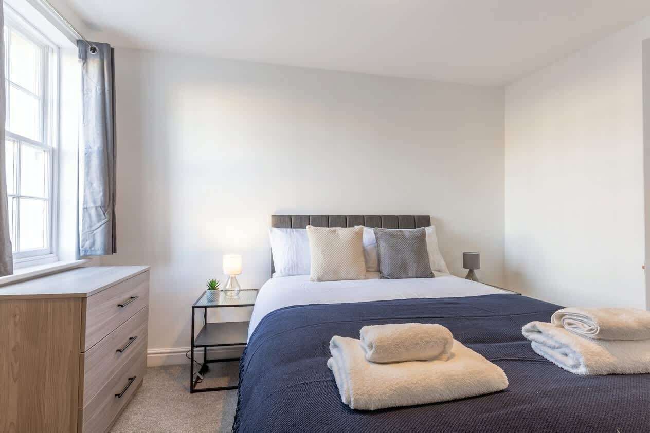 Un dormitorio con cama, mesitas de noche, cómoda y ventana con cortinas.
