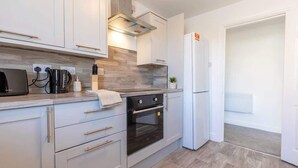A modern kitchen with white cabinetry, a built-in oven, and a stainless steel range hood. - Modern 2BR Sea View Flat on the Harbour (Whitehaven)