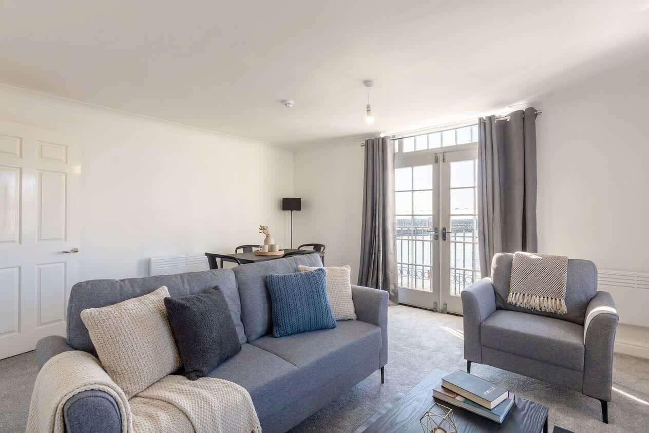 A modern living room with a grey sofa, a grey armchair, and a coffee table. There is a dining table with chairs in the background.