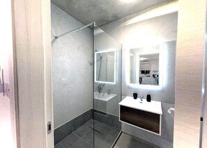 Ein modernes Badezimmer mit Duschkabine aus Glas, einem weißen Waschbecken und einem Spiegel mit integrierter Beleuchtung.
