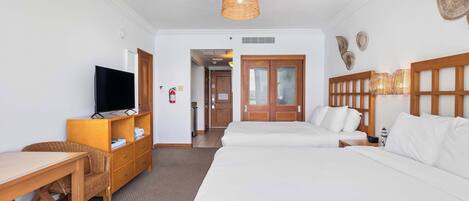 Une chambre d’hôtel avec un grand lit, un bureau avec une télévision, des meubles en osier et une tête de lit en bois.