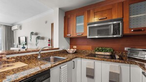 Een moderne keuken met granieten aanrechtbladen, roestvrijstalen apparatuur en houten kastjes.