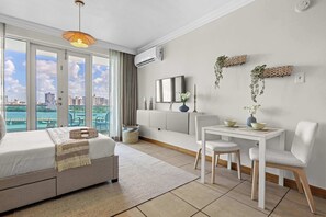 Ein Schlafzimmer mit Bett, Nachttisch und Blick auf die Stadt durch große Fenster.