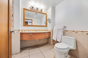 Ein Badezimmer mit einem Holzkosmetikschrank, einem großen Spiegel, einer Toilette und einem Handtuchhalter.