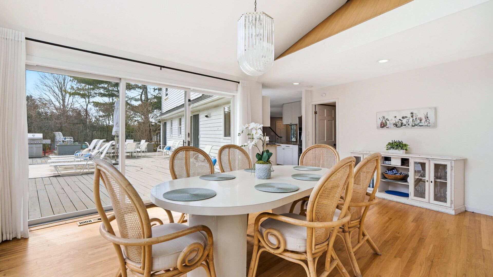 A dining area with a round table, wicker chairs, and a chandelier.