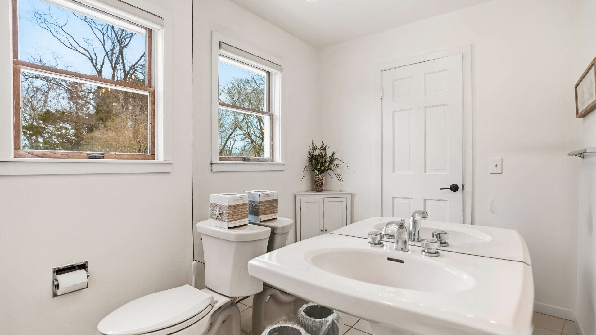 Ein Badezimmer mit Toilette, Bidet, Waschbecken und zwei Fenstern.