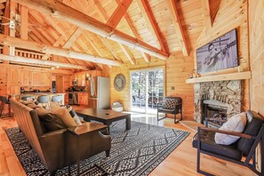 A log cabin interior with a dining area, kitchen, and fireplace. - The Johnny: Sleeps 16 w/ Brand-New Pool, Hot Tub, Firepit & Private Pond (Laurelville)