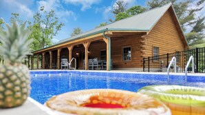 Una cabaña de madera con piscina, mobiliario exterior y un patio cubierto.