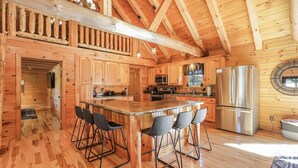 Interior de una cabaña de madera con cocina, barra y techos altos.