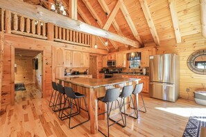 A wooden cabin interior with a kitchen, bar area, and high ceilings. - The Johnny: Sleeps 16 w/ Brand-New Pool, Hot Tub, Firepit & Private Pond (Laurelville)