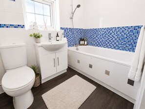 Moderni kylpyhuone, jossa on wc, pesuallas ja kylpyamme.