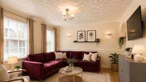 A living room with a red sofa, a round coffee table, a grey cabinet, and a TV mounted on the wall. - Manor Road Retreat | Modern | Sleeps 5 (London Colney)