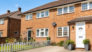 A two-story brick house with a white door, windows, and a small garden with potted plants. - Manor Road Retreat | Modern | Sleeps 5 (London Colney)