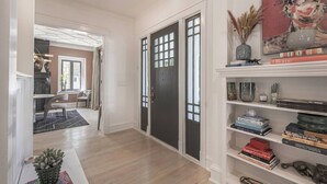 A hallway with a black door, a bookshelf with books, and a dining area with a table and chairs. - Loose Park Modern Mansion (Kansas City)