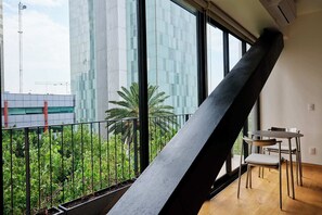 A modern room with a large window, a black metal structure, and a small table with chairs. - Colon: Loft with private balcony and Rooftop Pool (Ciudad de México)