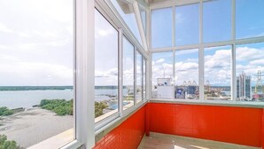 A room with large windows offering a view of a body of water and industrial structures. - Hotel Yubarta (Buenaventura)