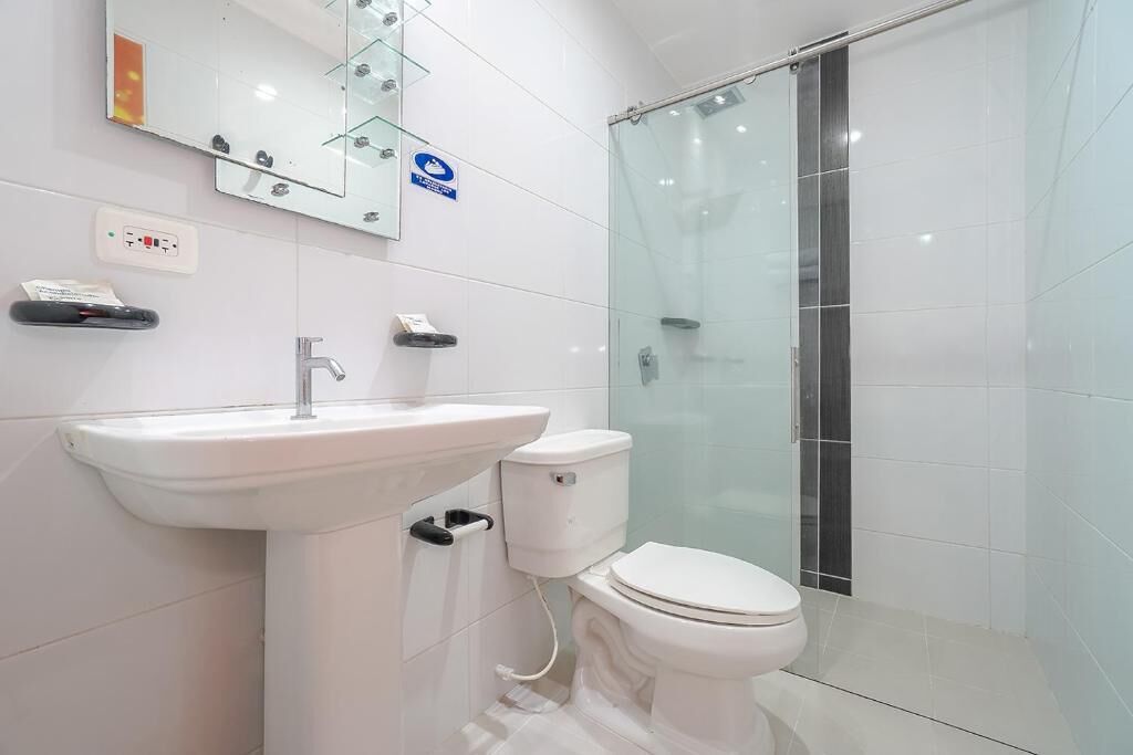 Un baño moderno con cabina de ducha de vidrio, un lavabo blanco y un inodoro.
