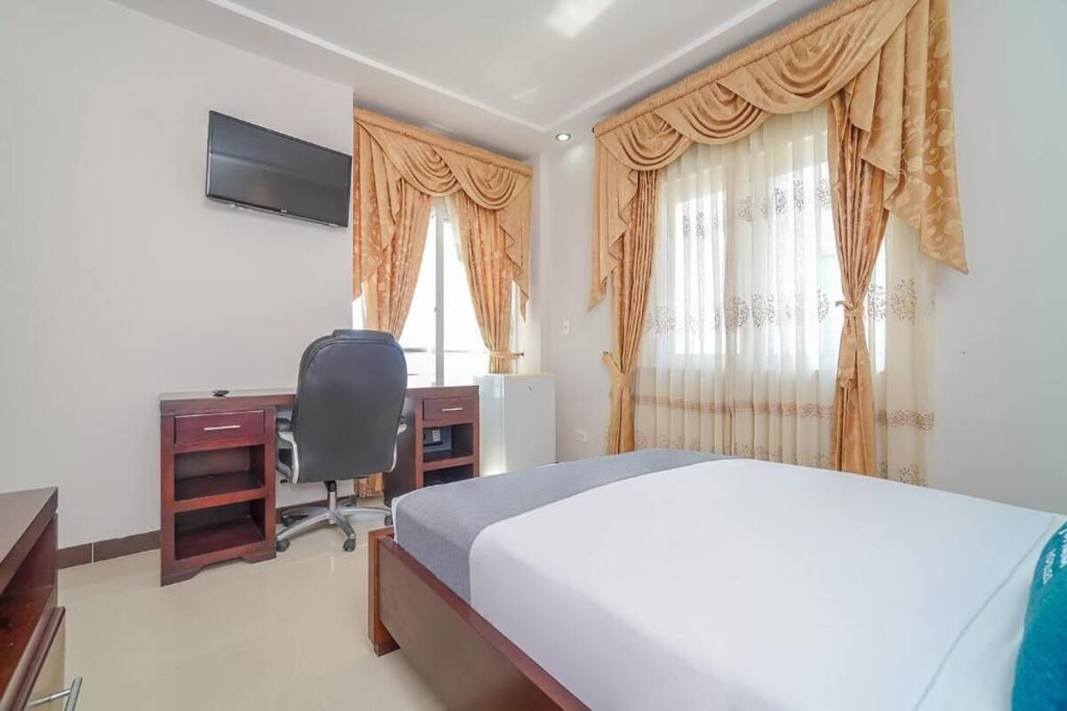 A hotel room with a bed, a desk with a chair, a television, and curtains.