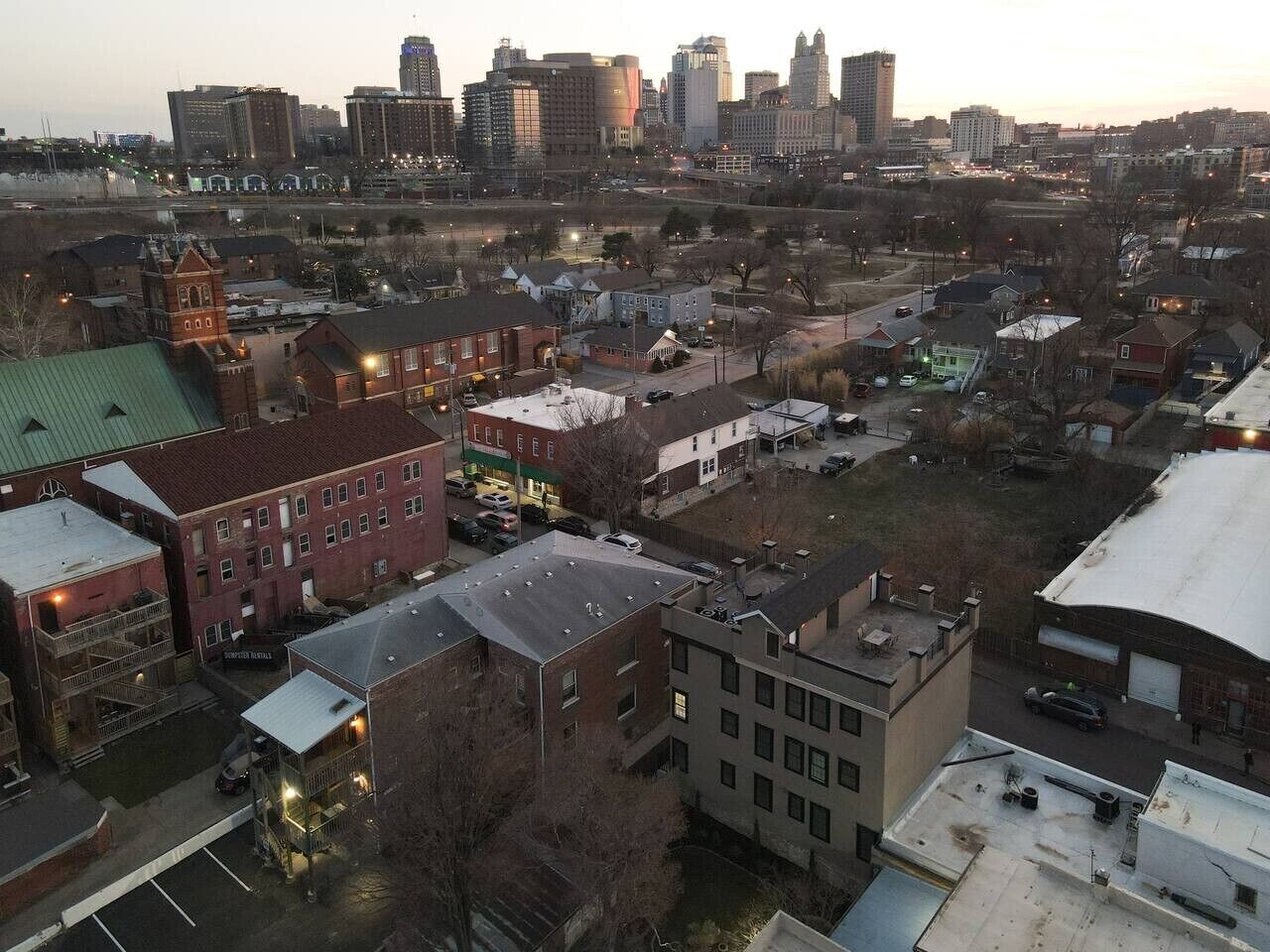 A cityscape with various buildings, including a prominent red brick building with a green roof and a smaller adjacent structure.